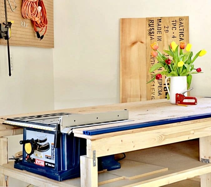 DIY Mobile workbench with table saw in garage corner with vase of tulips and red staple gun.