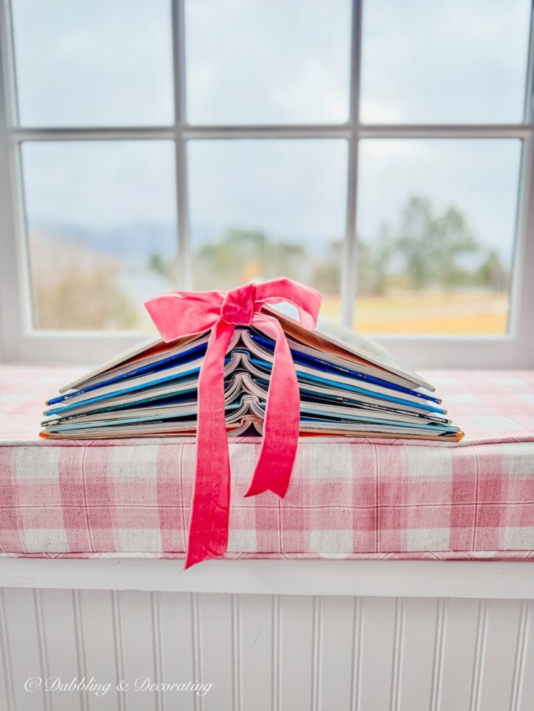 Book Christmas tree with bright pink ribbon on pink plaid window seat custom made cushions in front of window with rainy day mountain views.