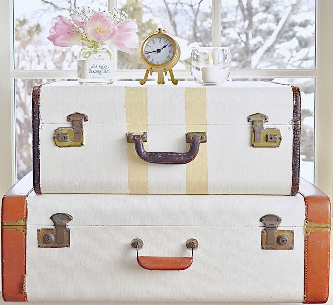 Painted Vintage suitcases stacked with clock and flowers in decor.