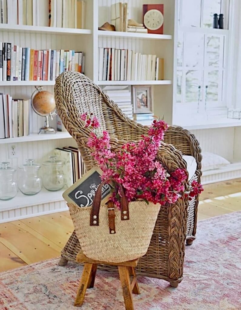 Sunroom makeover ideas with wicker chairs, spring flower bouquets on pink rug with built-in bookshelves.