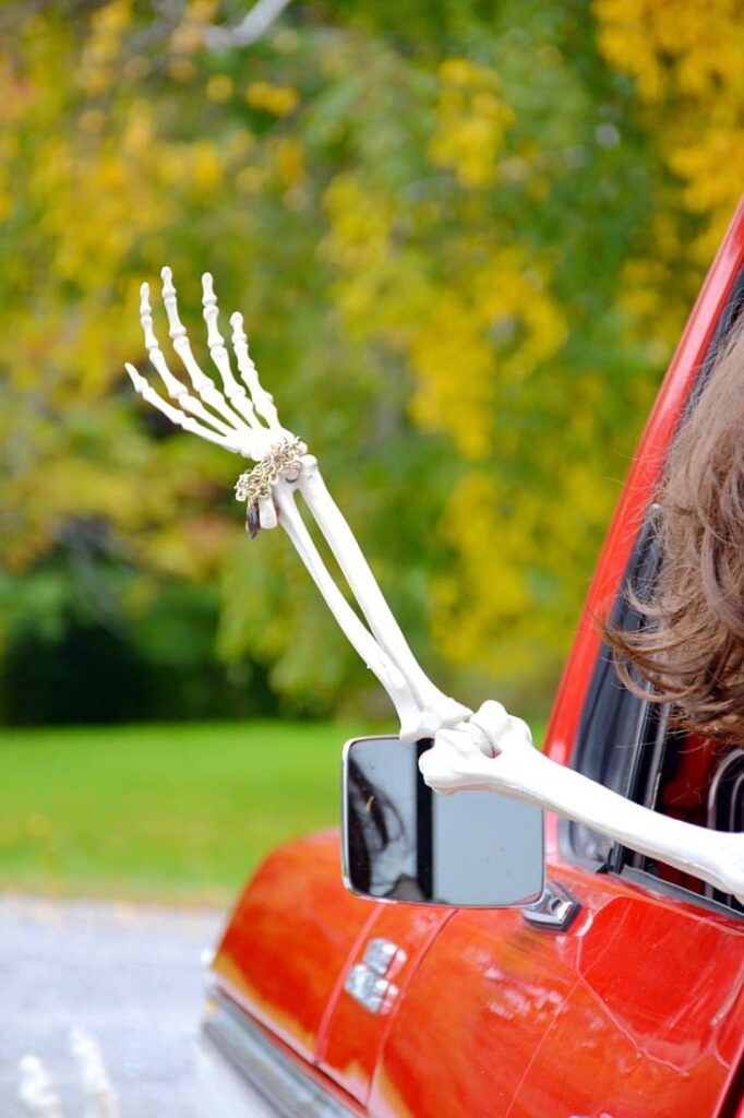 Halloween skeleton arm out the window of an old truck in the fall for outdoor Halloween decor.