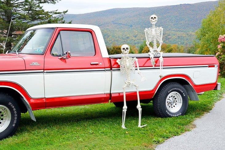 Halloween skeletons and Vintage Ford truck in the mountains. Two skeletons on and in front of an old red and white vintage Ford truck in the mountains during foliage.