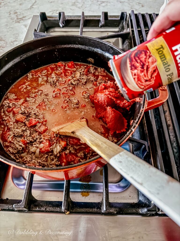 Hunt's tomato paste being dropped into a pasta bolognese sauce on stove with wooden spatula.
