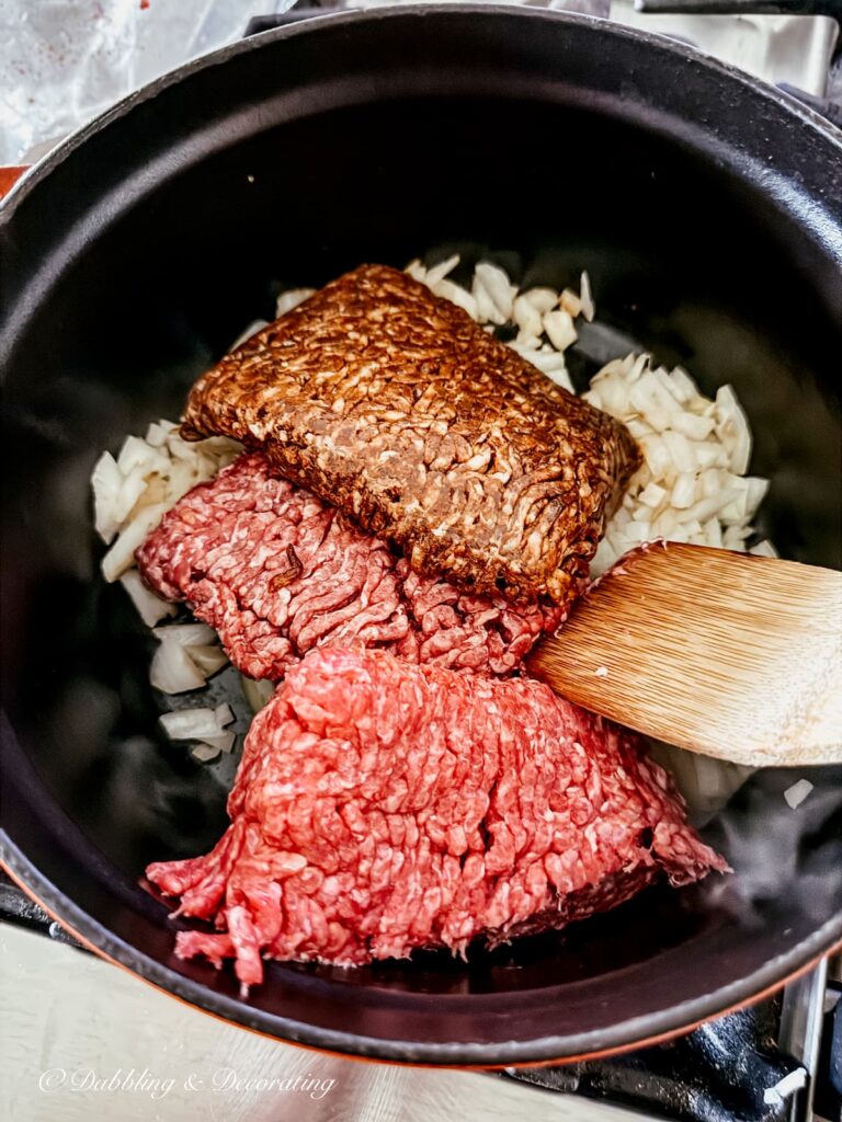 Authentic & Easy Bolognese Sauce Recipe Ground beef and sausage with onions in pot on stove with wooden spatula making pasta bolognese.