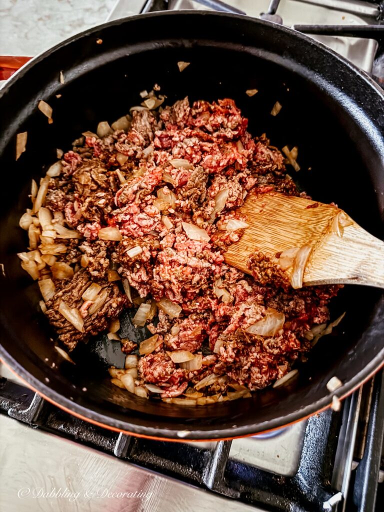 Ground beef, sausage, and onions with wooden spatula being stirred in pot on stove making pasta bolognese.