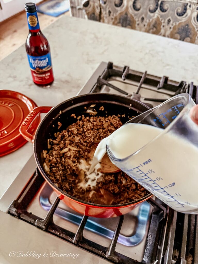 Adding milk to a pasta bolognese simmering on the stove.
