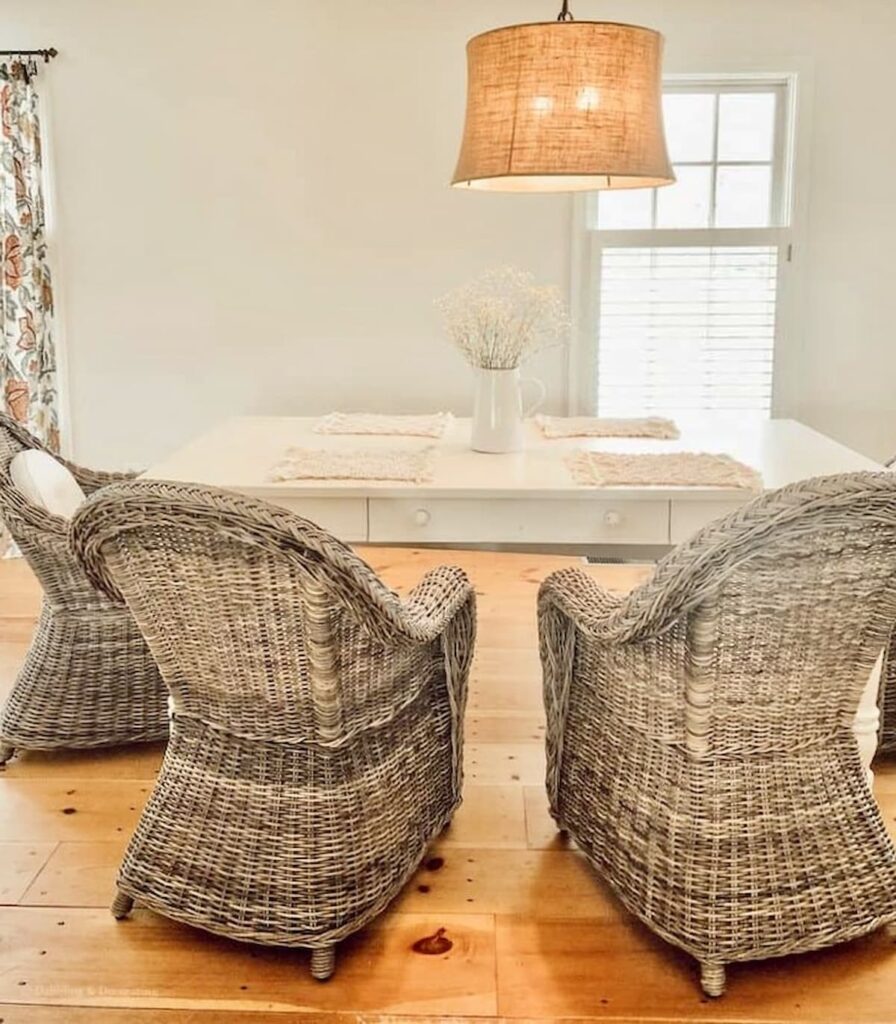 Vintage Dining Room with white farmhouse table and wicker chairs with hanging light and open white wall.