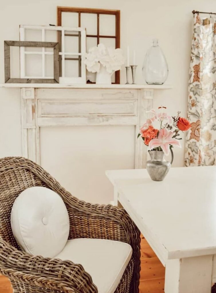 Vintage dining room neutrals with white faux mantel, layered old windows, wicker chair and vintage flower arrangement.