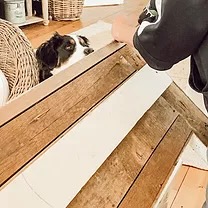 Back of wooden mantel man screwing in hook and screw to the backside with Bernese Mountain Dog looking on.