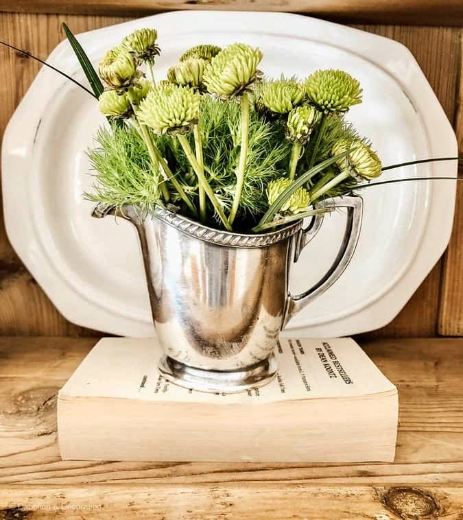Silver pitcher with greenery in vintage hutch on book