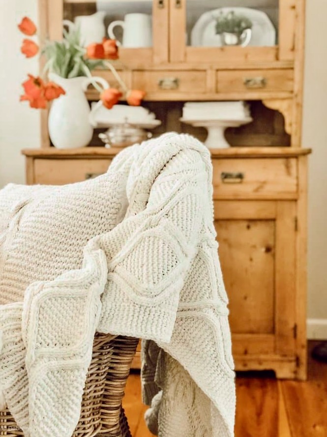 Wicker Chair with Blanket in front of vintage cabinet.