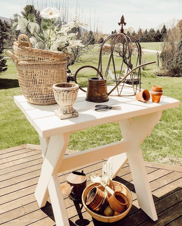 White DIY garden table ideas outdoors with baskets, terracotta pots, urns and watering can.