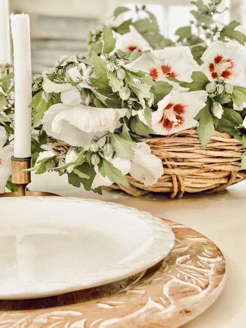 Close up of Rose of Sharon flower bouquet in basket with white plate and wooden table charger.