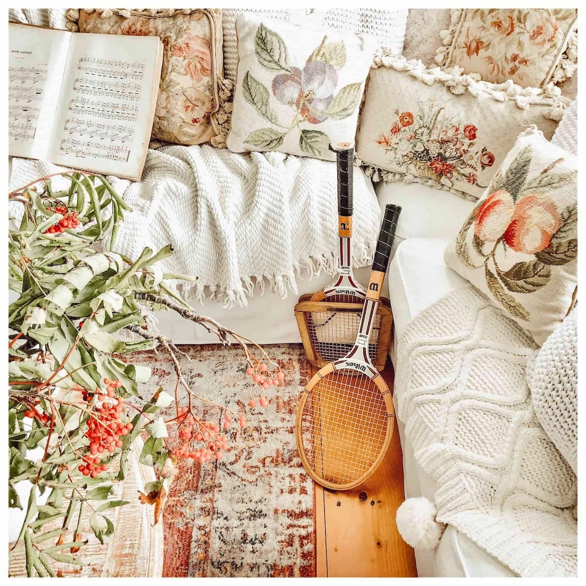 Vintage tennis racket decor in sunroom with needlepoint pillows and soft pastel colors.