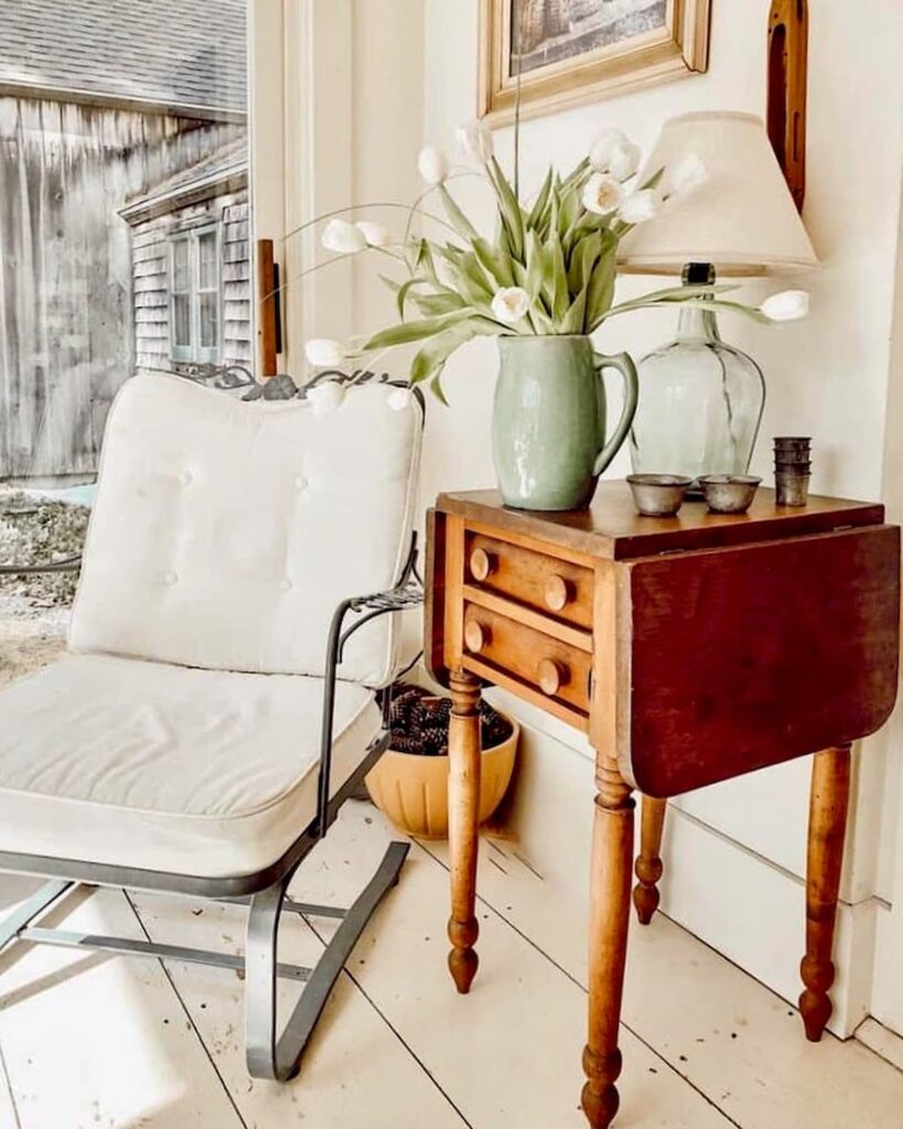 Sunroom in old Raeside-Dame home with antique wooden table and white chair with bouquet of white tulips and white flooring.