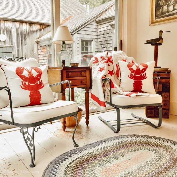 Sunroom in old Raeside-Dame Home with braided rug, white chairs with lobster pillows and red and white quilt with antique tables.