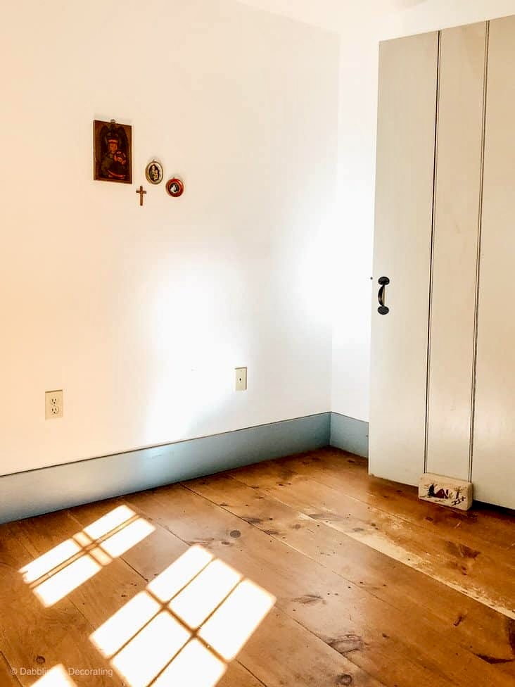 Empty guest bedroom with white walls and open latched door with dark wood flooring and antique pictures on wall.