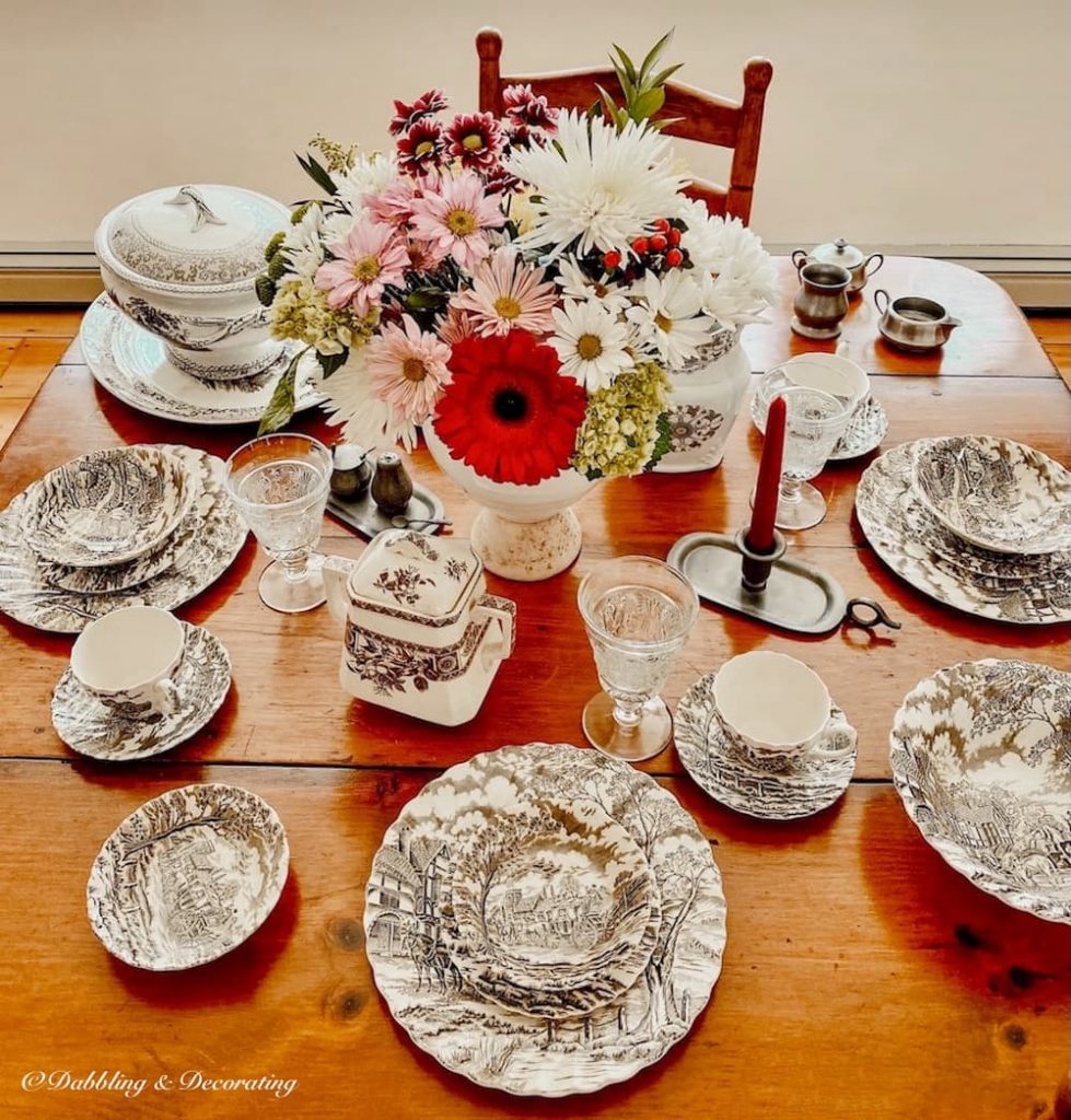 Collection of brown and white transferware on dining room table with Thanksgiving centerpiece of flowers.