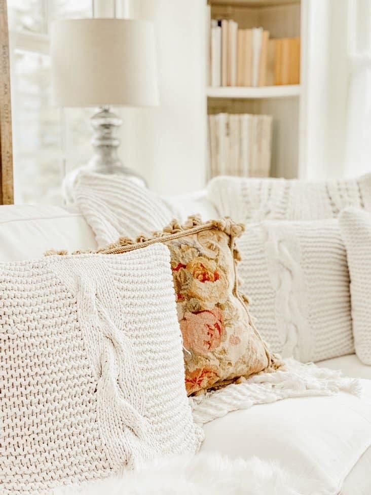 Winter white pillows mixed with an embroidered neutral pillow on white sectional sofa in cozy winter white decor ideas.