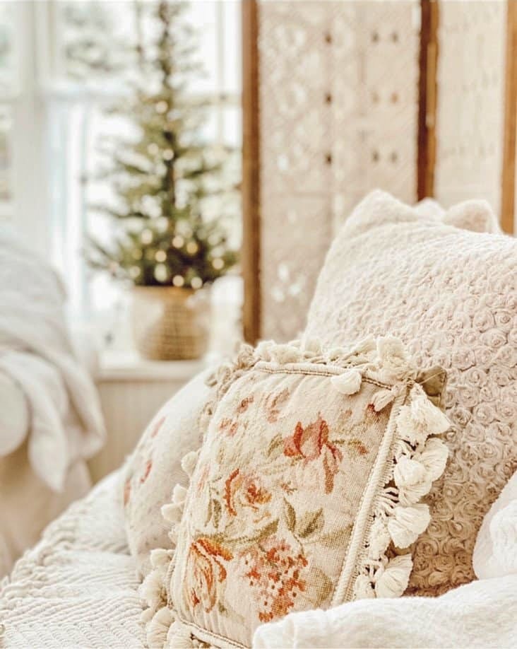Winter white decor ideas with vintage needlepoint pillows on white sunroom coach with small Christmas tree in window.