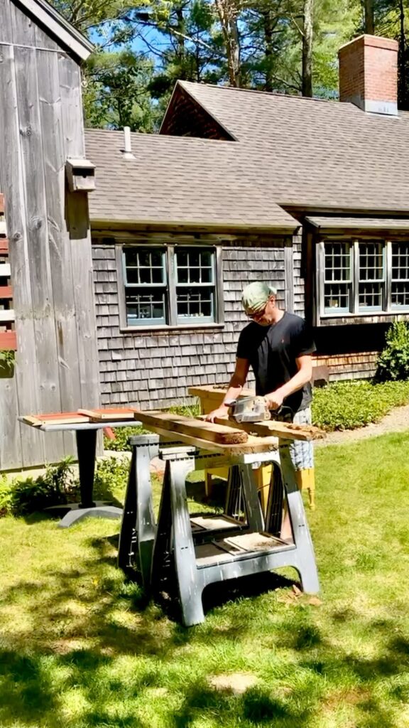 Man sawing barn wood with table saw outdoor on saw horses in backyard.