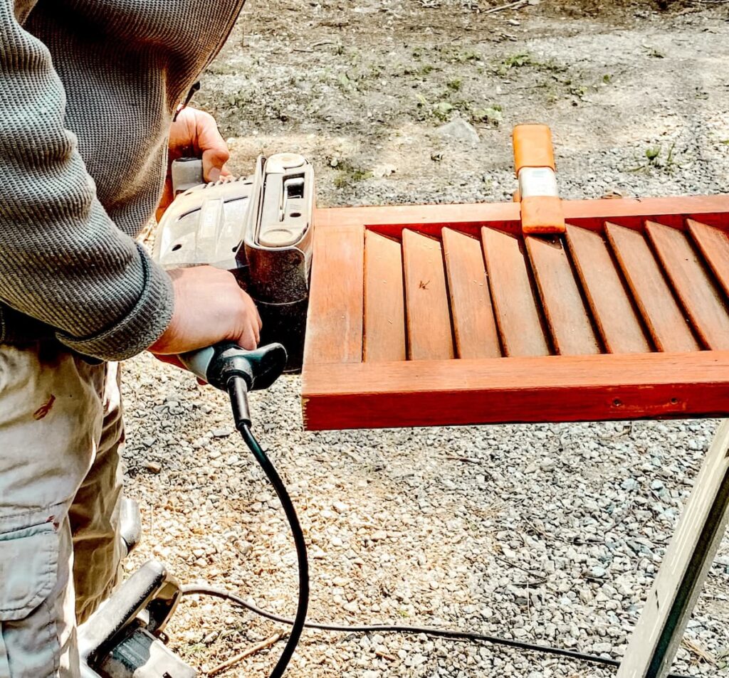 Man sanding an old orange shutter.