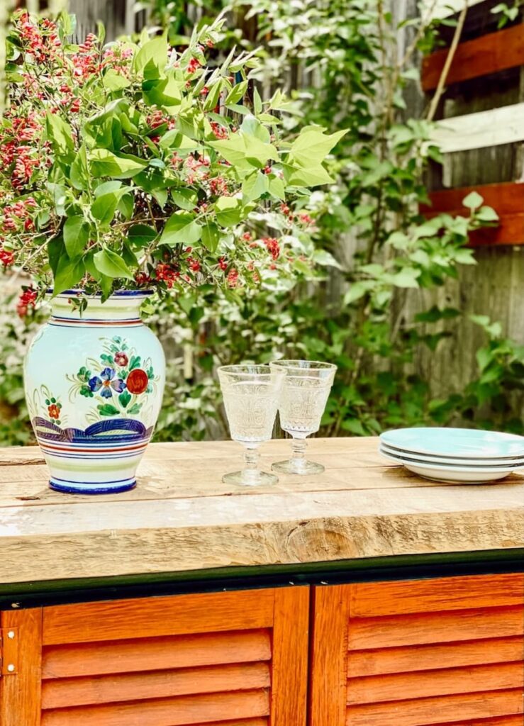 DIY grill station wooden top with glassware, dishes and bouquet of summer flowers.