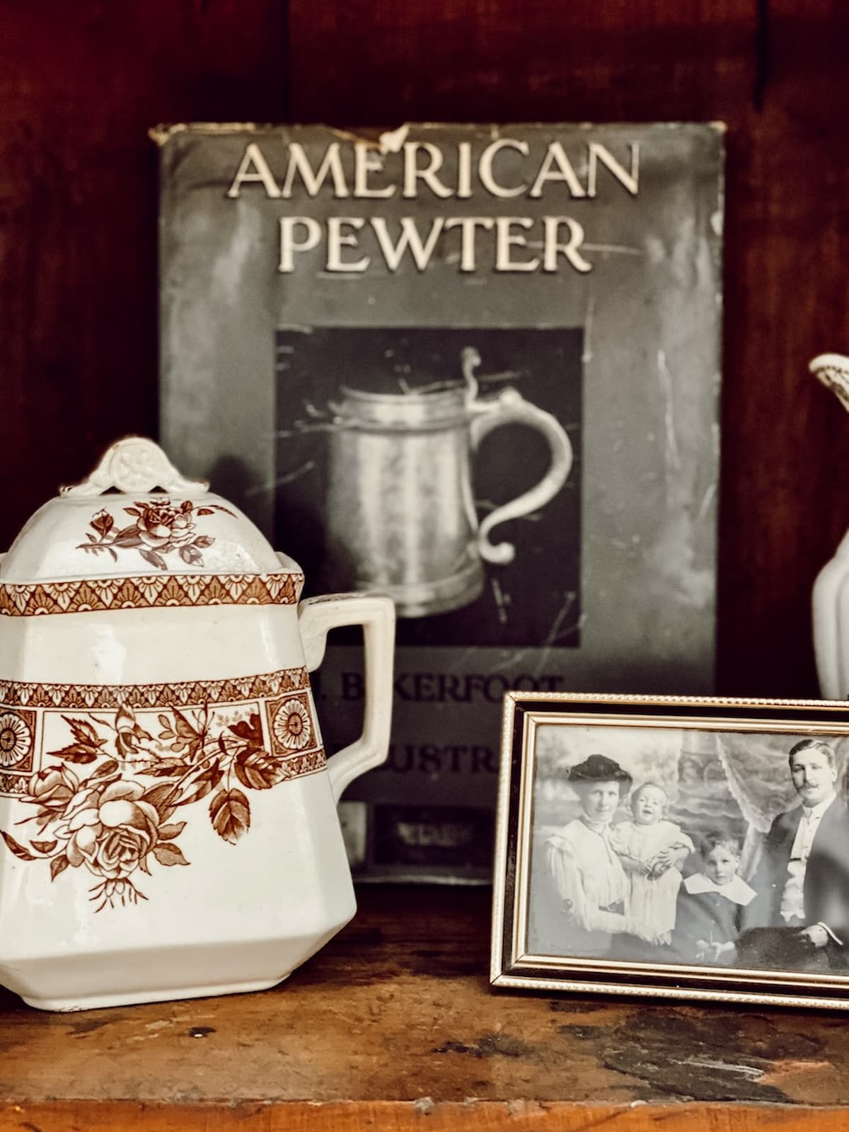 Antique American Pewter Decor book in hutch with antique brown and white transferware pitcher and old heirloom photo.