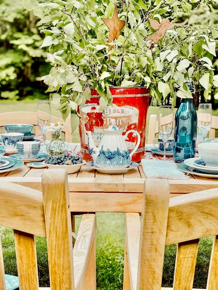 Red galvanized bucket with green branches on outdoor Patriotic alfresco tablescape.