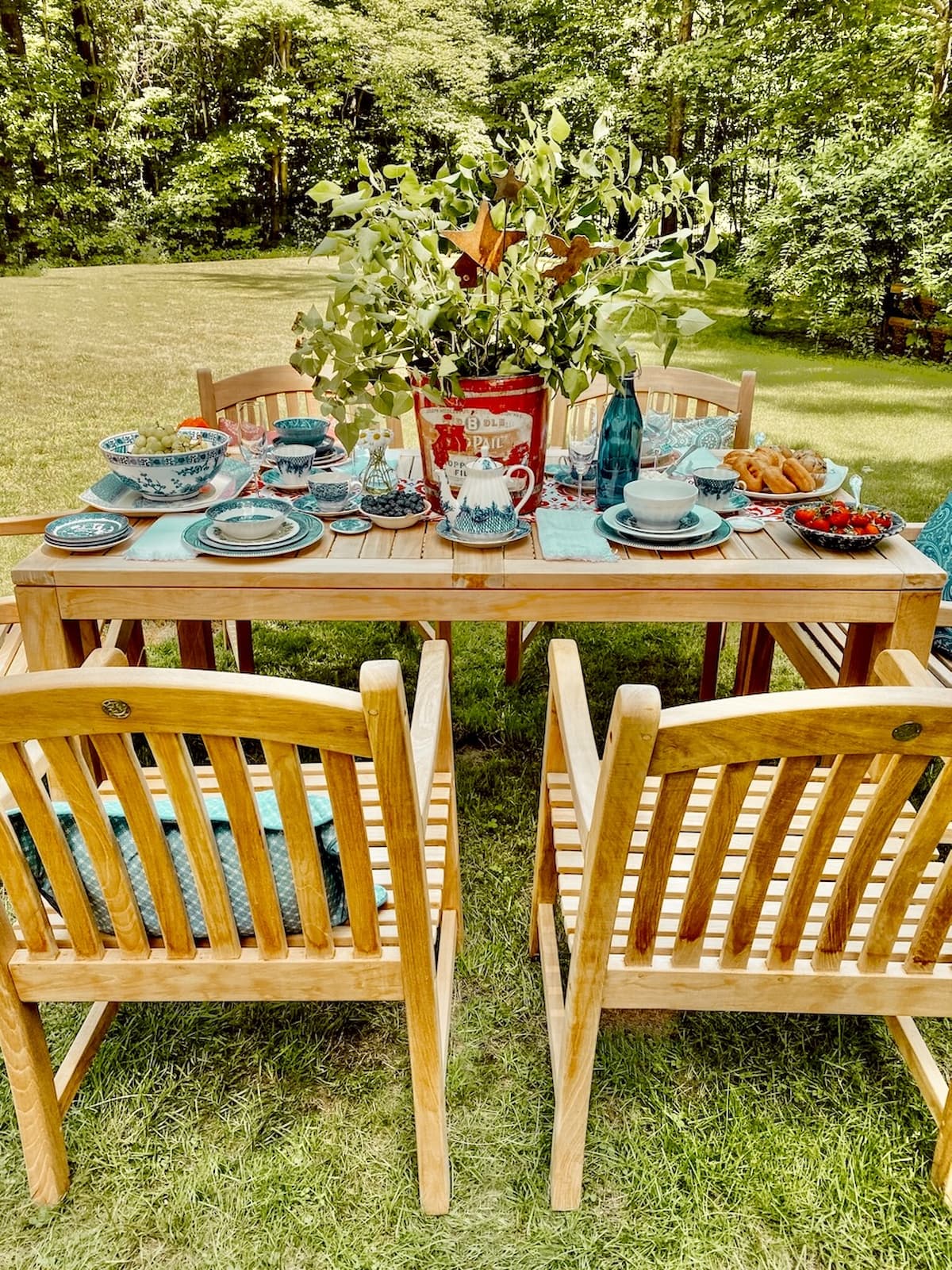An Alfresco Summer Breakfast Table Outdoor teak table set for breakfast with red galvanized bucket centerpiece and red, white, and blue place settings for summer.
