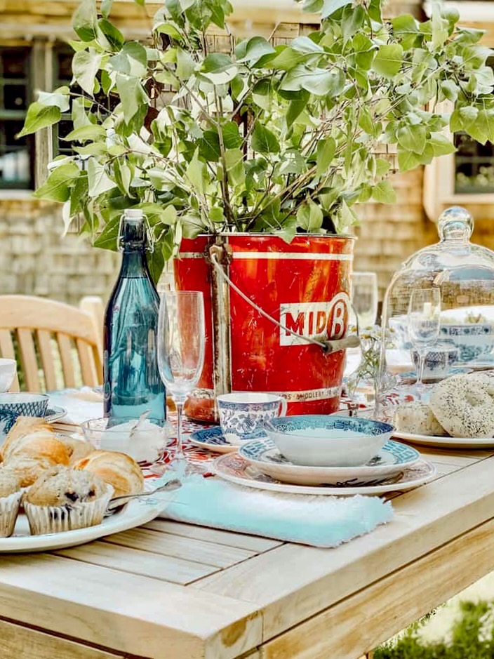 Red galvanized bucket with branches with green leaves on Patriotic alfresco tablescape.