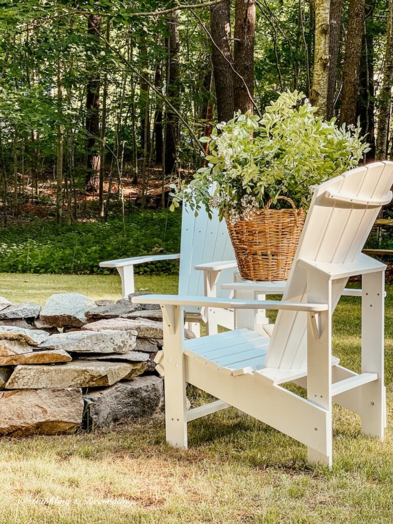 Backyard DIY stone fire pit with white Adirondack chairs and a basket full of roadside flowers in the summer