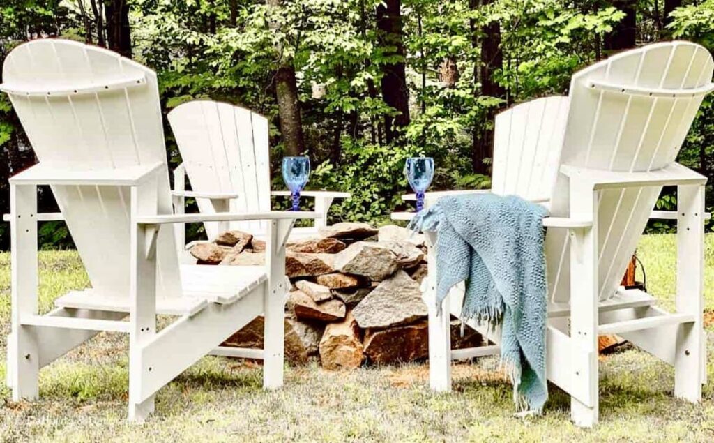 DIY stone fire pit with white Adirondack upright chairs in backyard.