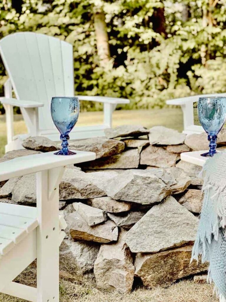 DIY Stone Fire Pit with White Adirondack Chairs with Blue glasses and Blue blanket in backyard.