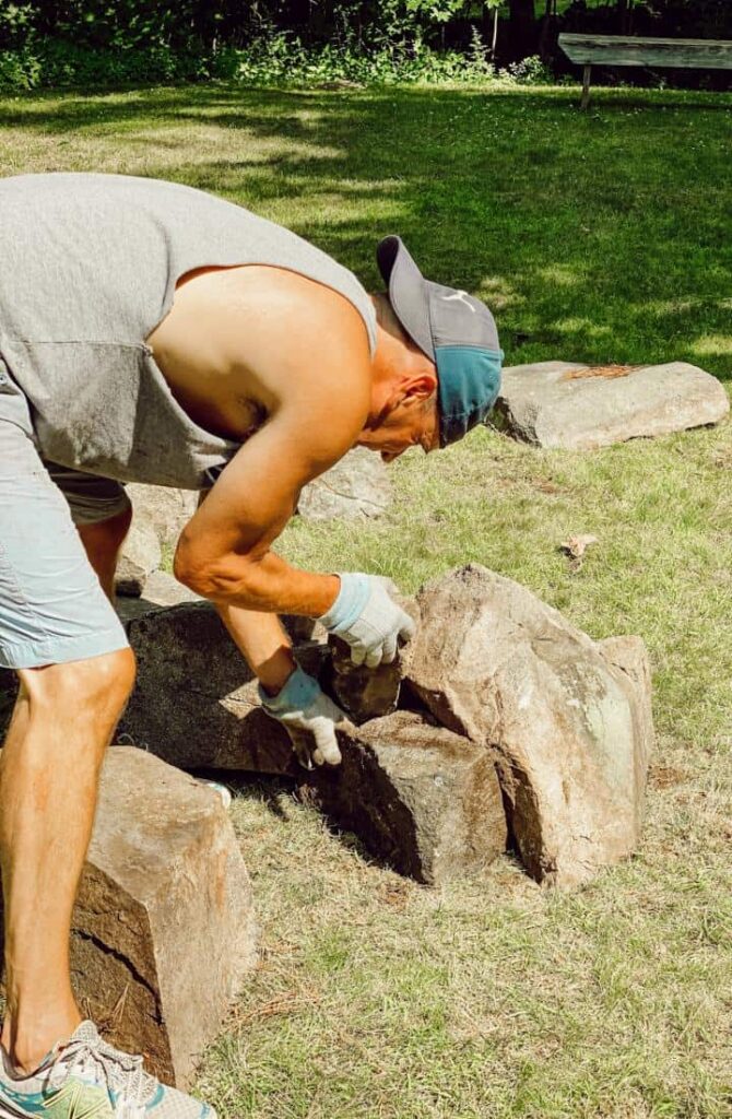 Man arranging large rocks in backyard to create a DIY fire pit.