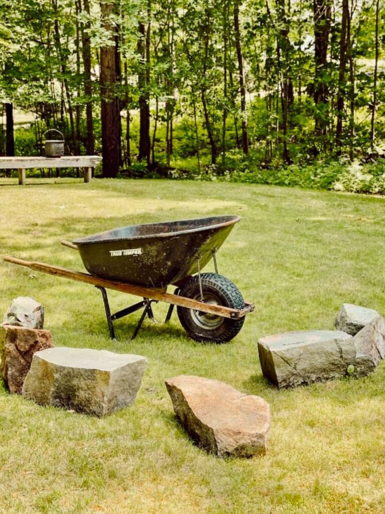Wheelbarrow in backyard with large rocks to create a DIY fire pit.