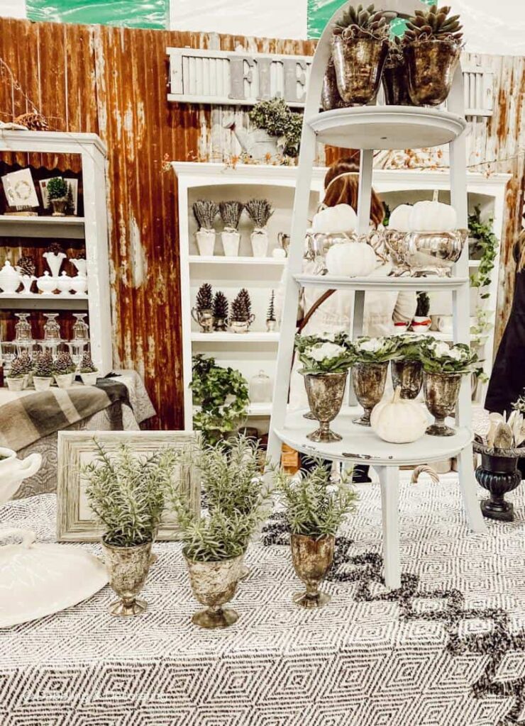 Silver vases with evergreens and white pumpkins in vintage booth.