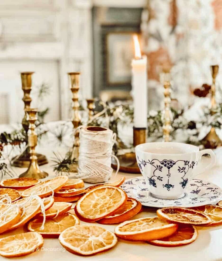 Dried oranges with twine, lit vintage brass candlestick candles, a tea cup on table after baking for Christmas tree ornaments.