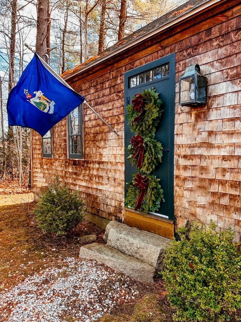 Three wreaths on green front door on Maine cedar shakes home with Maine flag and burgundy bows.
