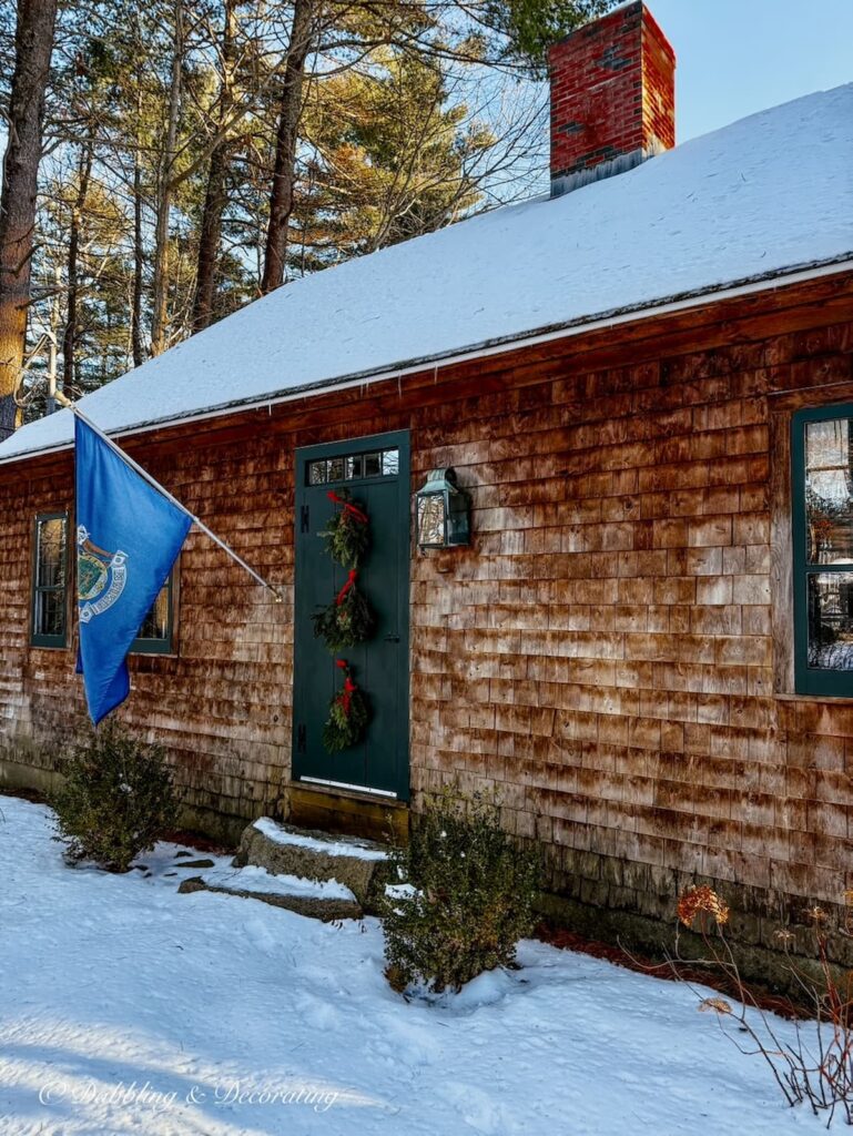 Three Christmas swags with red bows hanging on the front door of a cedar shakes home in Maine.
