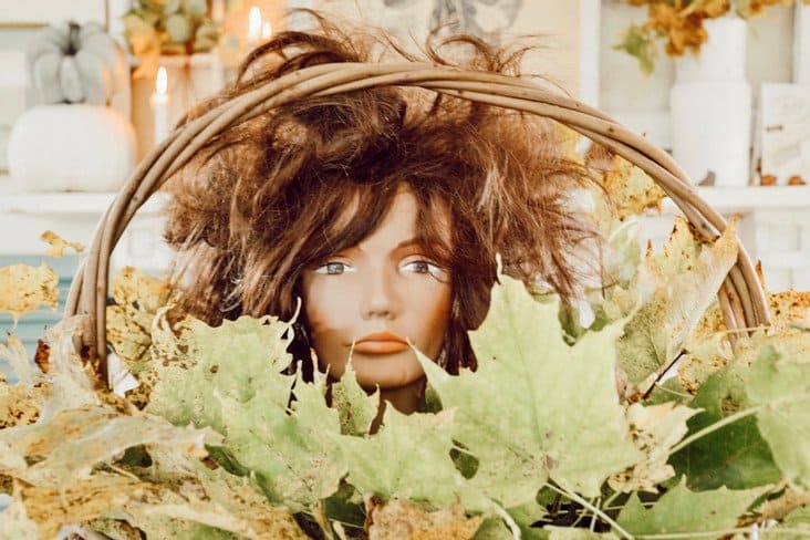 Mannequin head in basket of leaves.