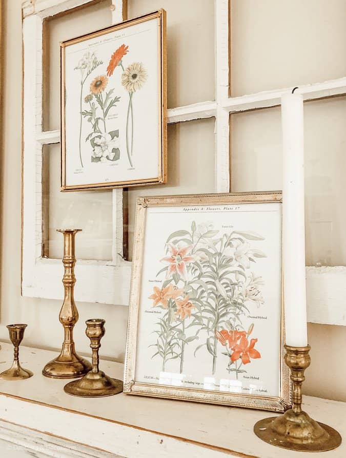 Vintage fireplace mantel with spring botanical framed prints and brass candlesticks.