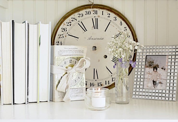 Decorated bookshelf with vintage finds clock face, books candle pictures and more.