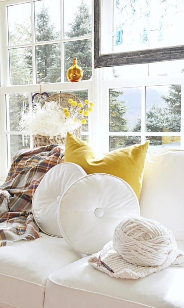 A vintage white couch adorned with yellow pillows, elegantly positioned in front of a window.