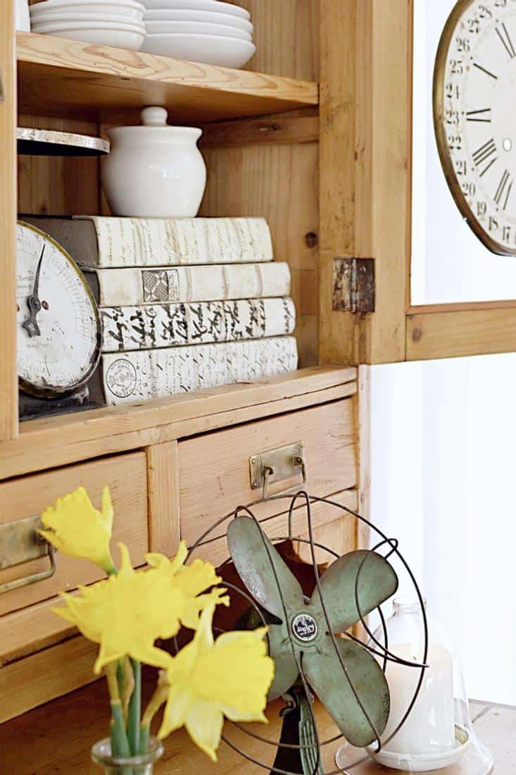 Vintage fan, scale, books, clock in an old wooden hutch.