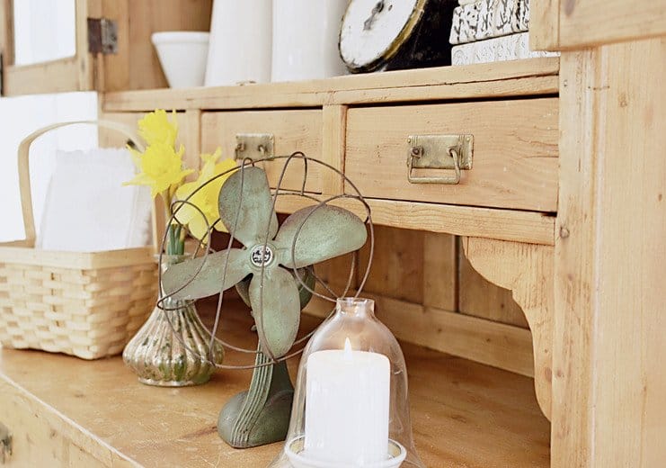 Vintage green fan, daffodils, basket, candle, scale, books and whites in an old wooden hutch.