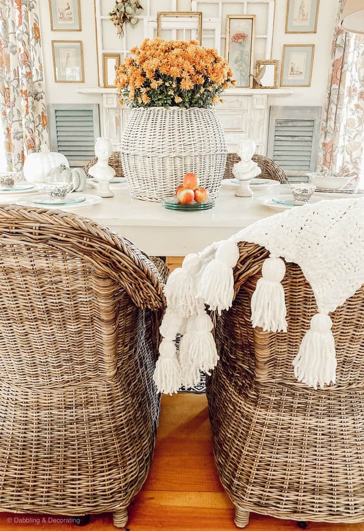 Thanksgiving centerpiece with orange mums in white round basket on table in farmhouse style dining room.