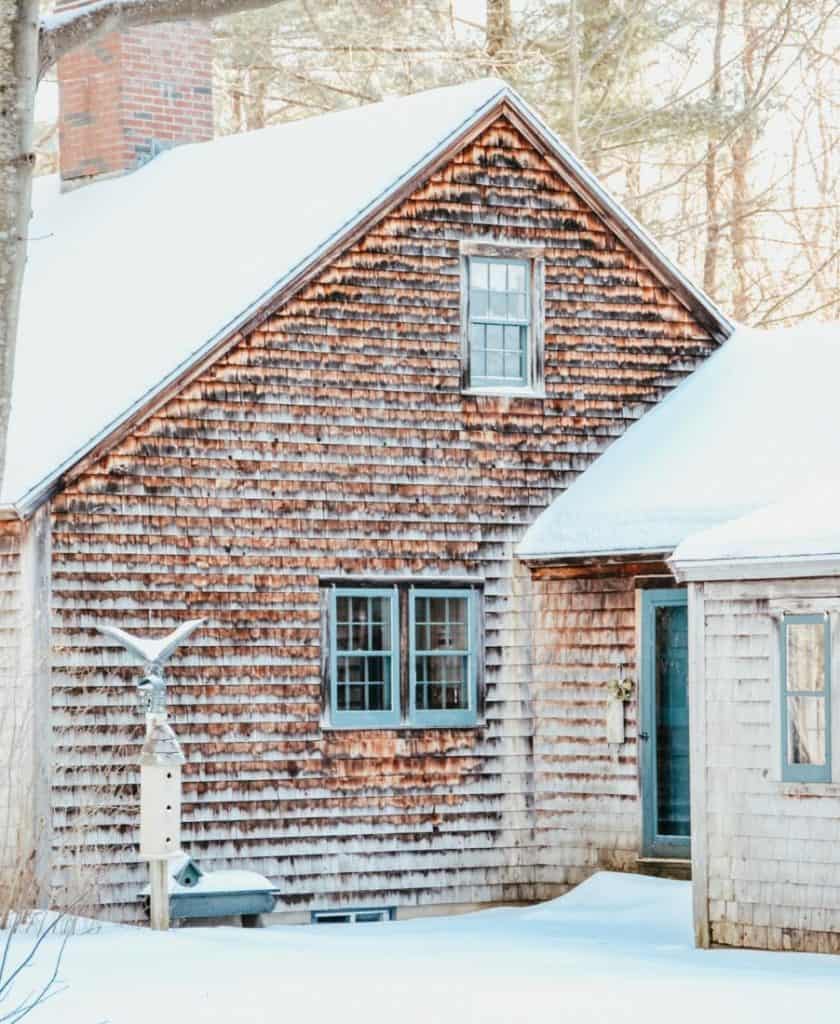 A vintage house in the woods with snow on the roof.