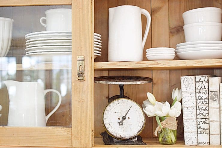 Vintage wooden hutch with white pottery, vintage scale, tulips, and books.