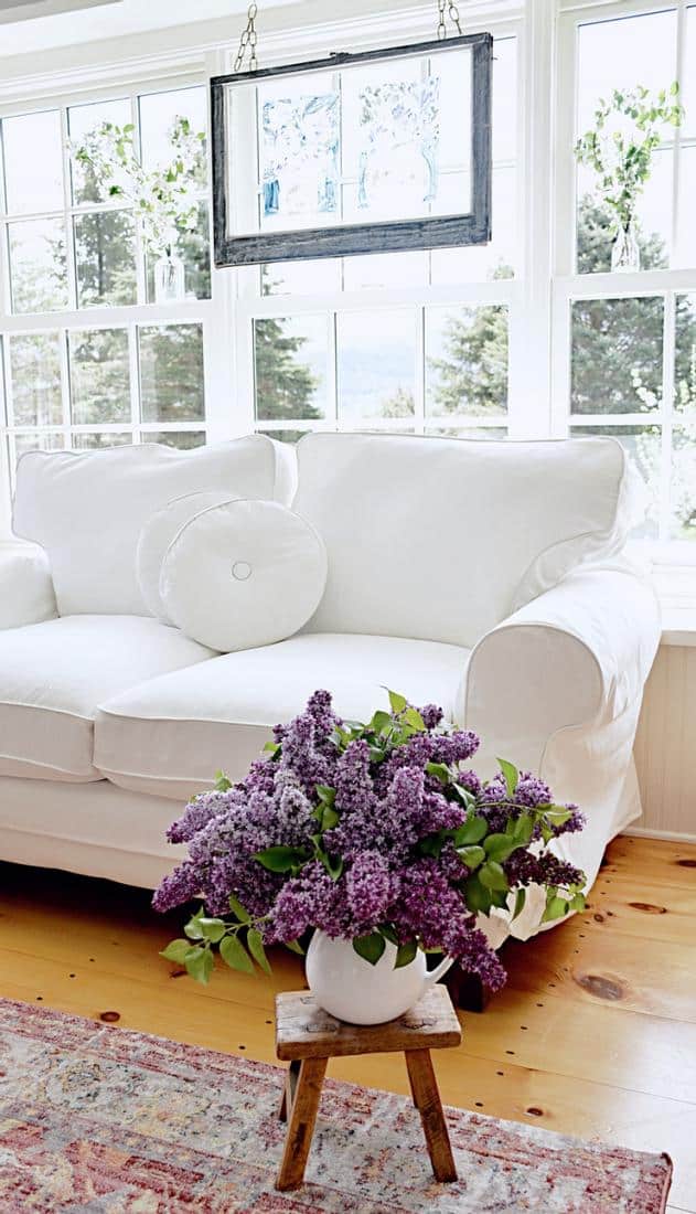 Sunroom windows with vintage hanging window with white flowers in jars and white loveseat.